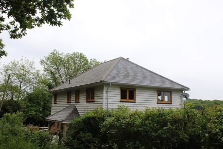 Two-storey weatherboard house with a light grey slate hipped roof in a woodland setting
