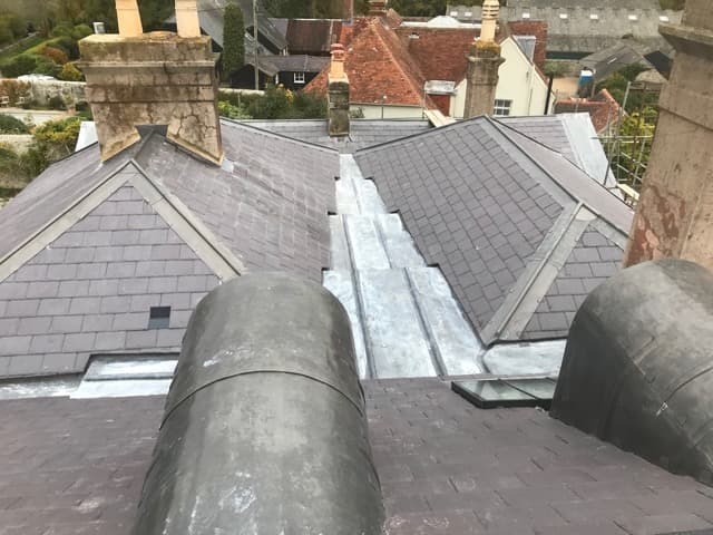 Grey slate hipped roof with lead valleys and flashing, village rooftops behind