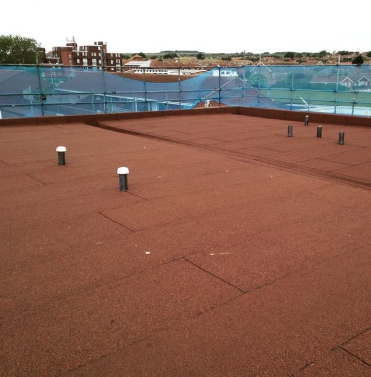 Completed red mineral-felt flat roof with vent pipes, rooftops behind