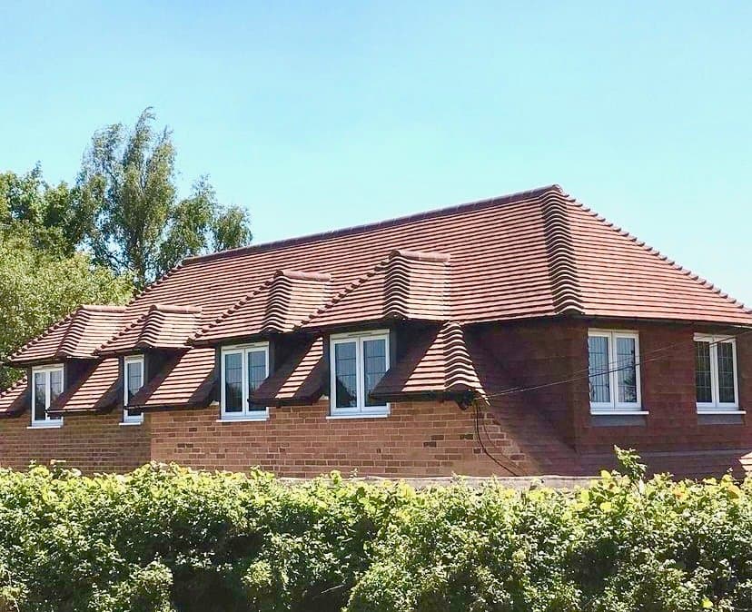 Brick house with a red clay tiled roof and a row of catslide dormer windows under a blue sky